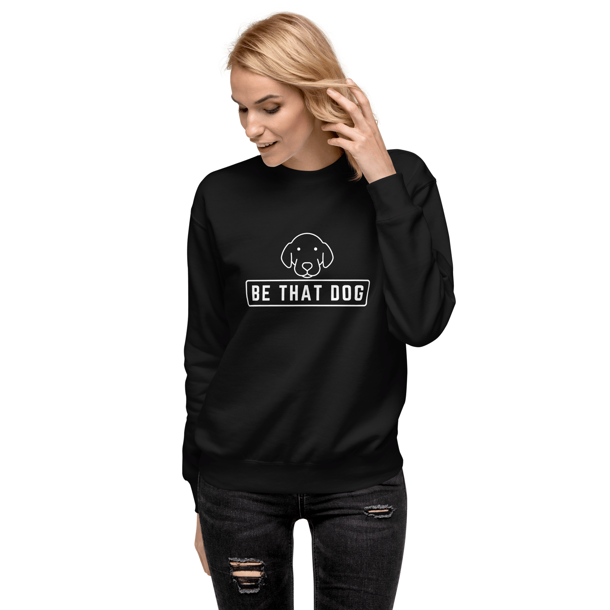 A woman in a THiNK LiKE A DOG® sweatshirt, perfect for dog lovers, with an illustration and "BE THAT DOG" text. She adjusts her hair while looking down against a sleek black background.