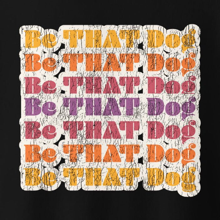 The THiNK LiKE A DOG® "Be THAT Dog Retro Sweatshirt" features vibrant text on a black, cracked texture background in shades of yellow, orange, purple, and red. Made from 100% cotton face, this '70s style unisex sweater is perfect for dog lovers wanting to make a bold statement.