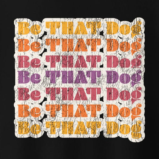 The THiNK LiKE A DOG® "Be THAT Dog Retro Sweatshirt" features vibrant text on a black, cracked texture background in shades of yellow, orange, purple, and red. Made from 100% cotton face, this '70s style unisex sweater is perfect for dog lovers wanting to make a bold statement.