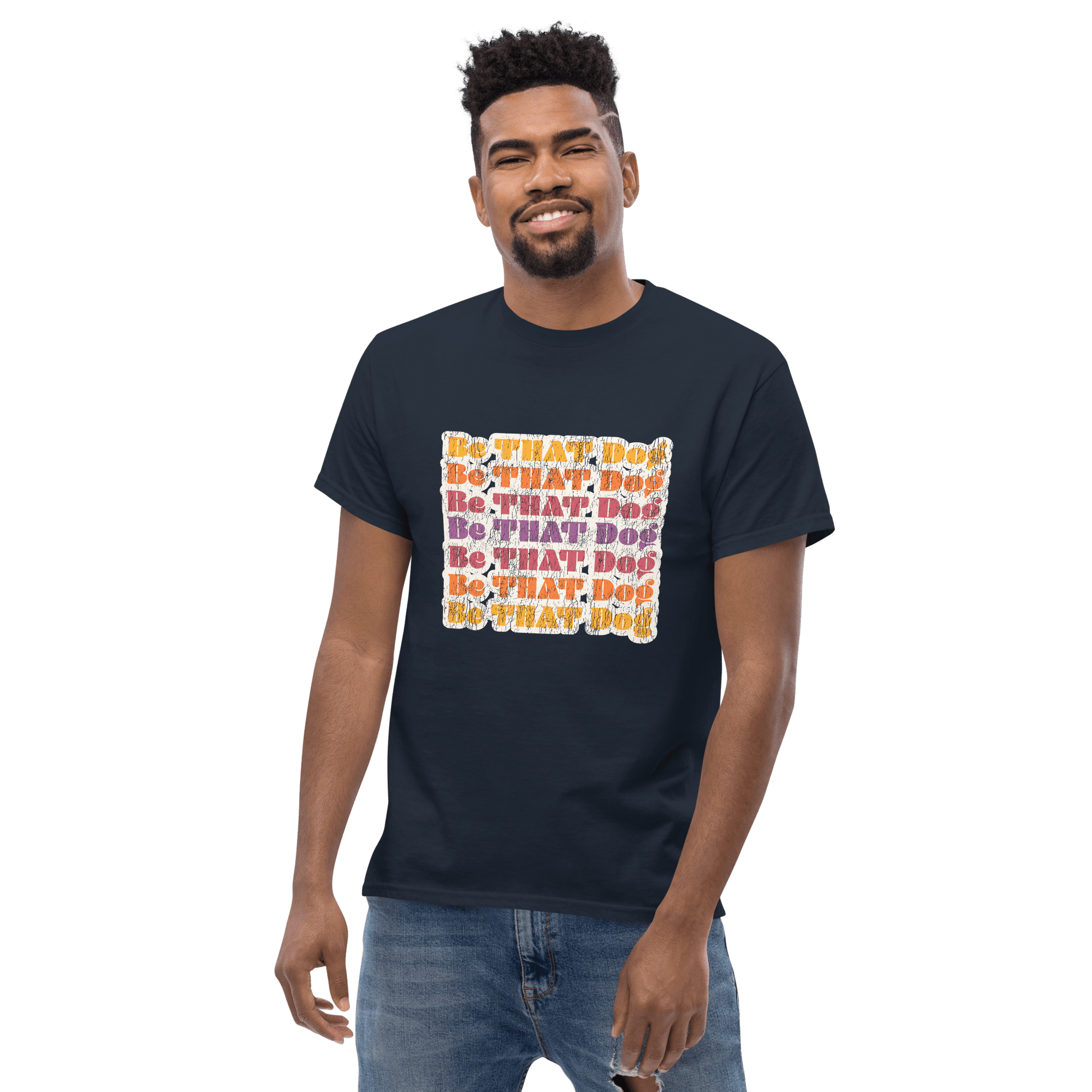 A man wears the 'Be That Dog Retro Unisex Tee,' a '70s-inspired shirt by THiNK LiKE A DOG®, featuring vibrant "Be That Dog" text on a black background, perfect for dog enthusiasts.