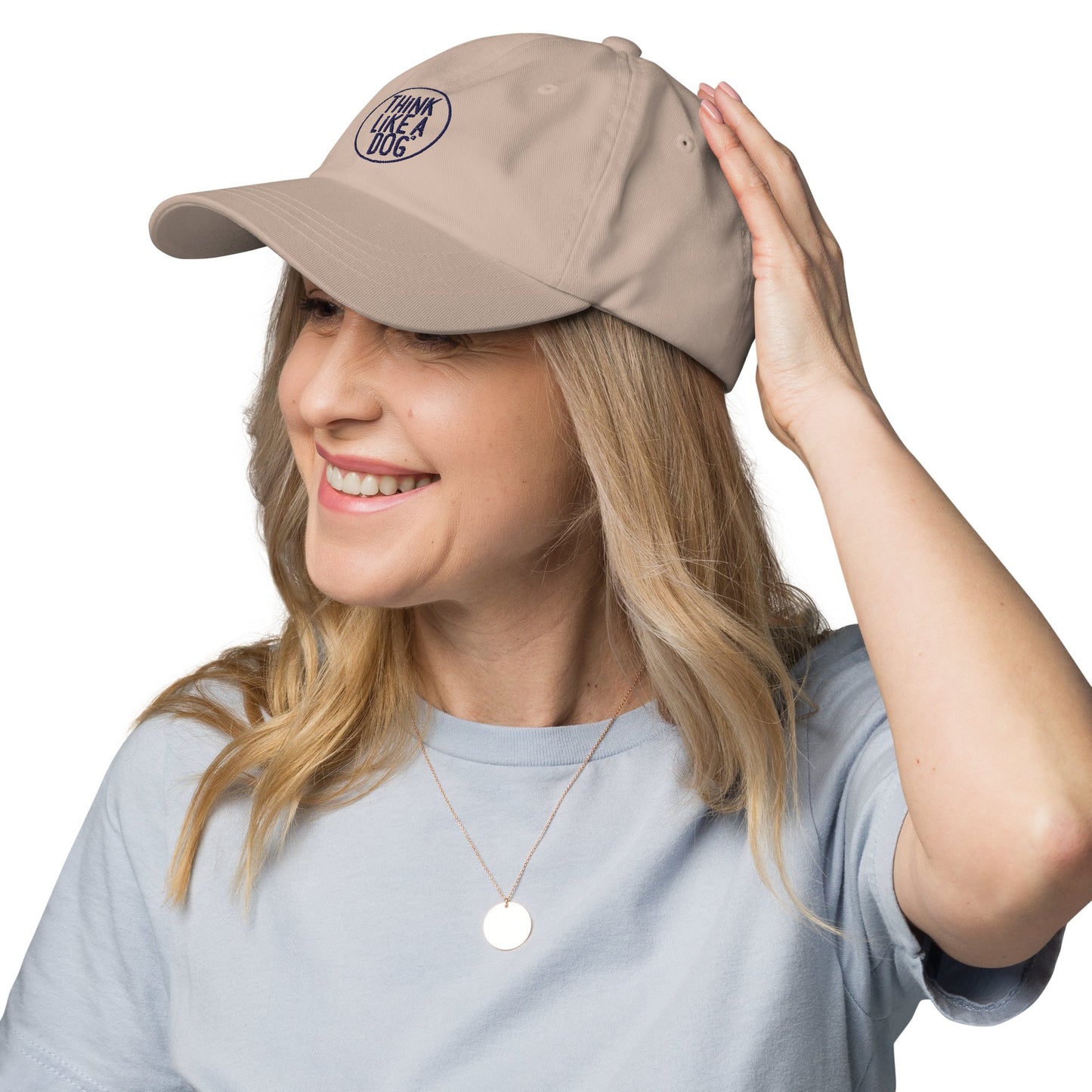 A person with long blonde hair, wearing a Think Like a Dog Circle Logo Classic Navy Dad Hat by THiNK LiKE A DOG®, and a light blue shirt, smiles and looks to the right.