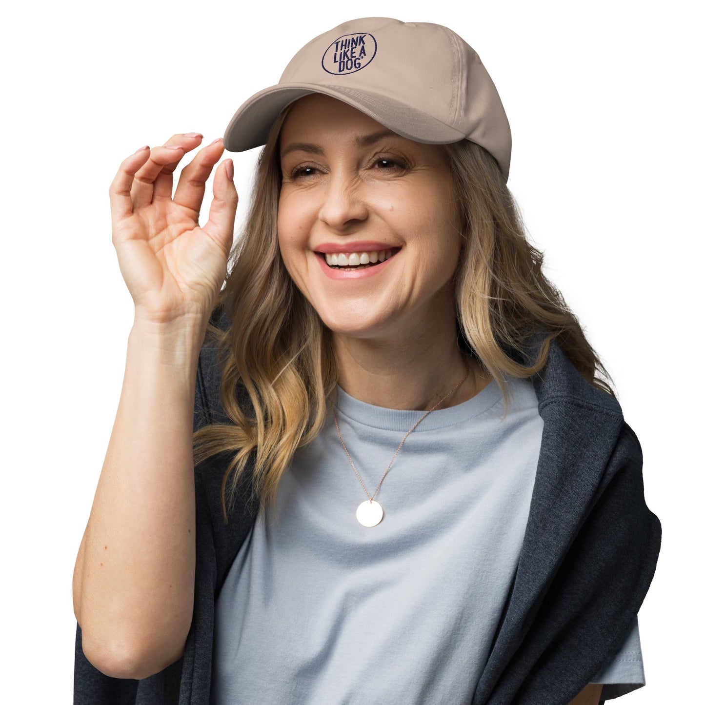 A woman smiles beneath a Classic Navy Dad Hat - Think Like a Dog Circle Logo by THiNK LiKE A DOG®, ideal for dog lovers. She pairs it effortlessly with a light blue shirt and a dark gray shawl, posed against a white background.