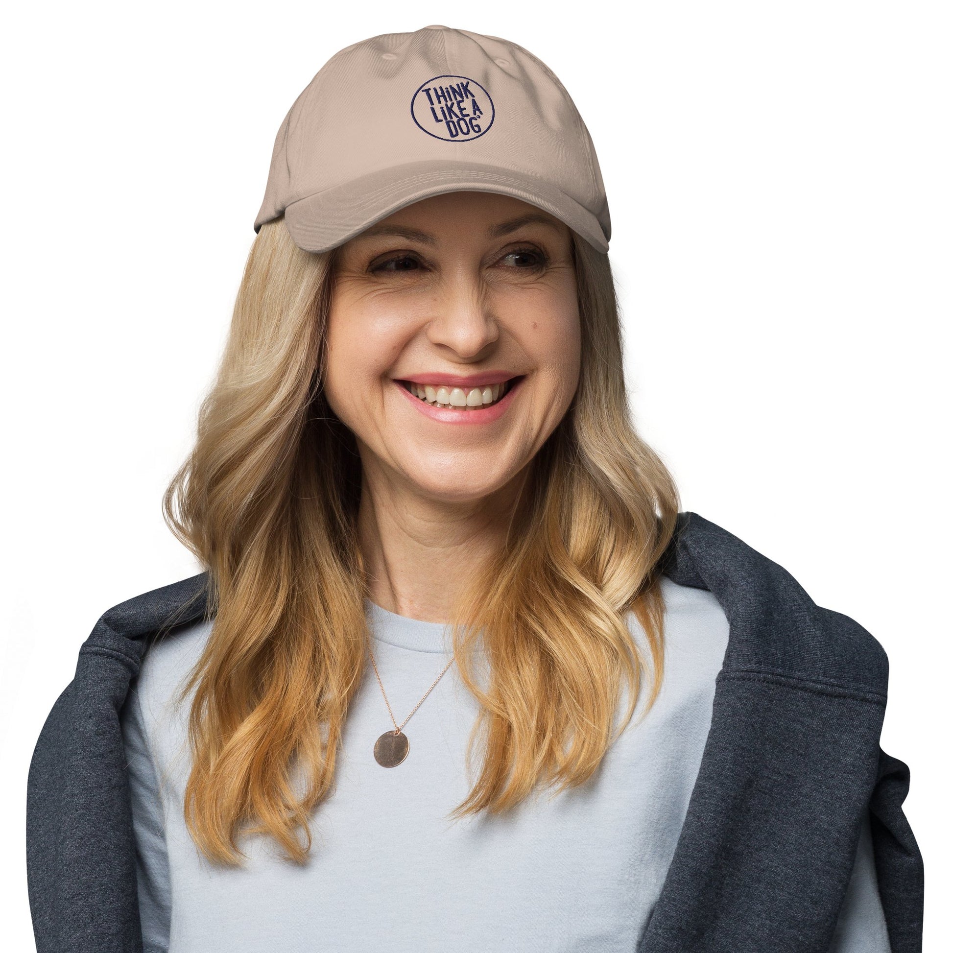 Smiling woman wears a Classic Navy THiNK LiKE A DOG® Dog Lover Dad Hat—a great gift for dog lovers—paired with a light blue shirt, dark jacket over her shoulders, and a round necklace.