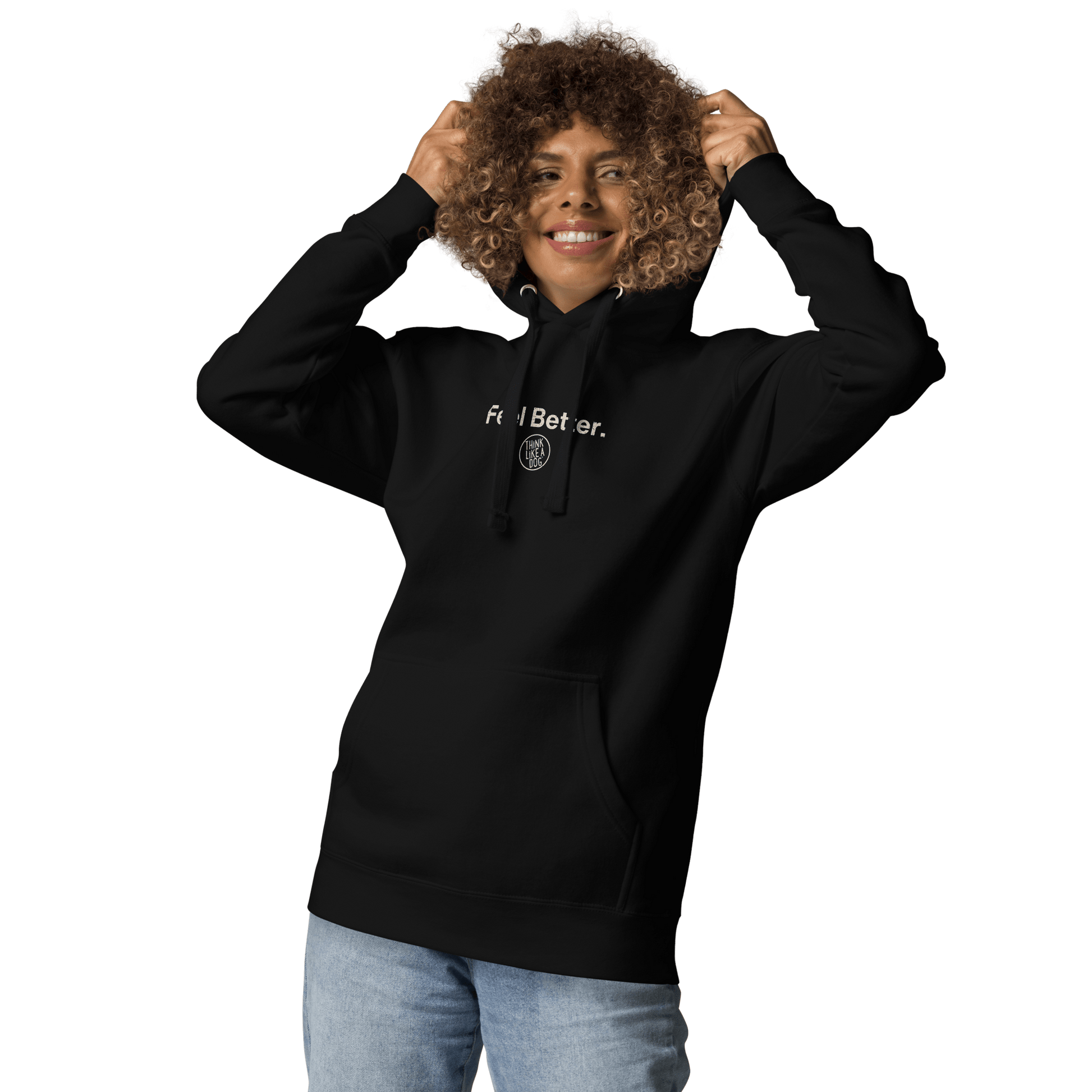 A person smiles while wearing a black THiNK LiKE A DOG® "Feel Better Dog Lover Hoodie," holding the hood strings against a black background. This cozy comfort is perfect for pet parents and dog moms.