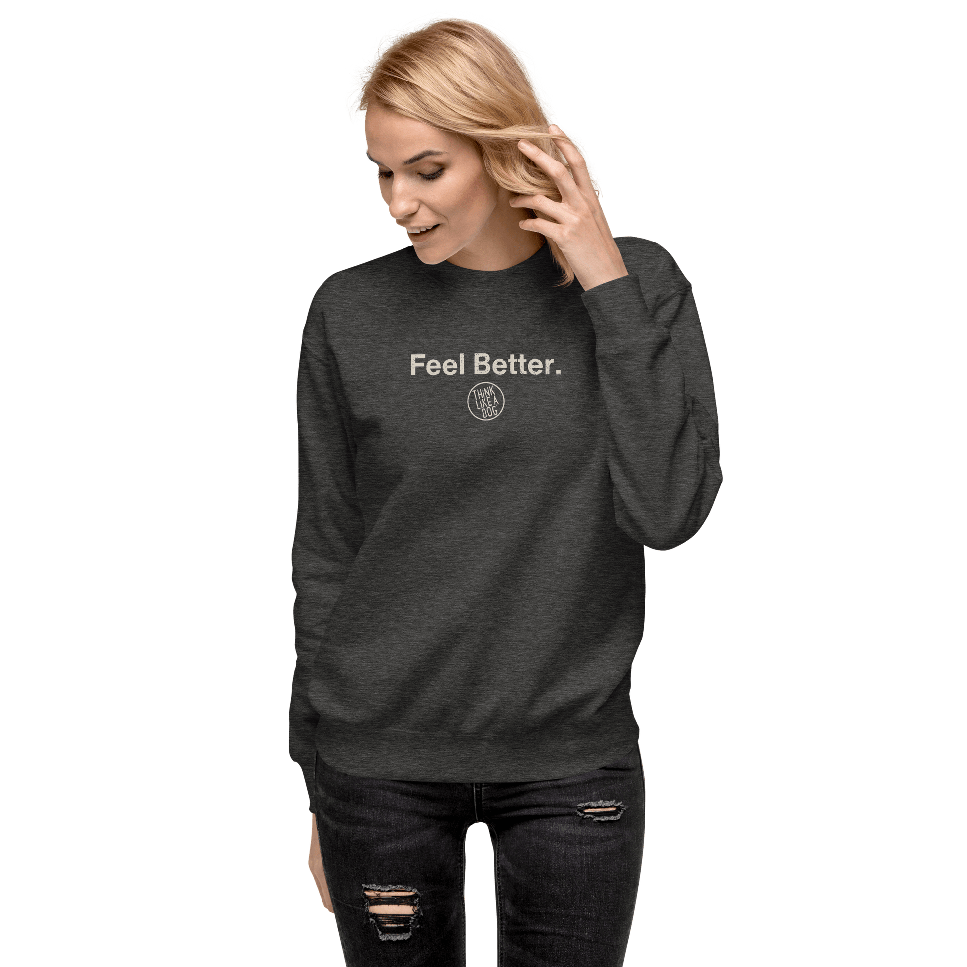A person in a dark gray "Feel Better Dog Lover" sweatshirt by THiNK LiKE A DOG®, supporting mental wellness, adjusts their hair while wearing ripped jeans against a black background.
