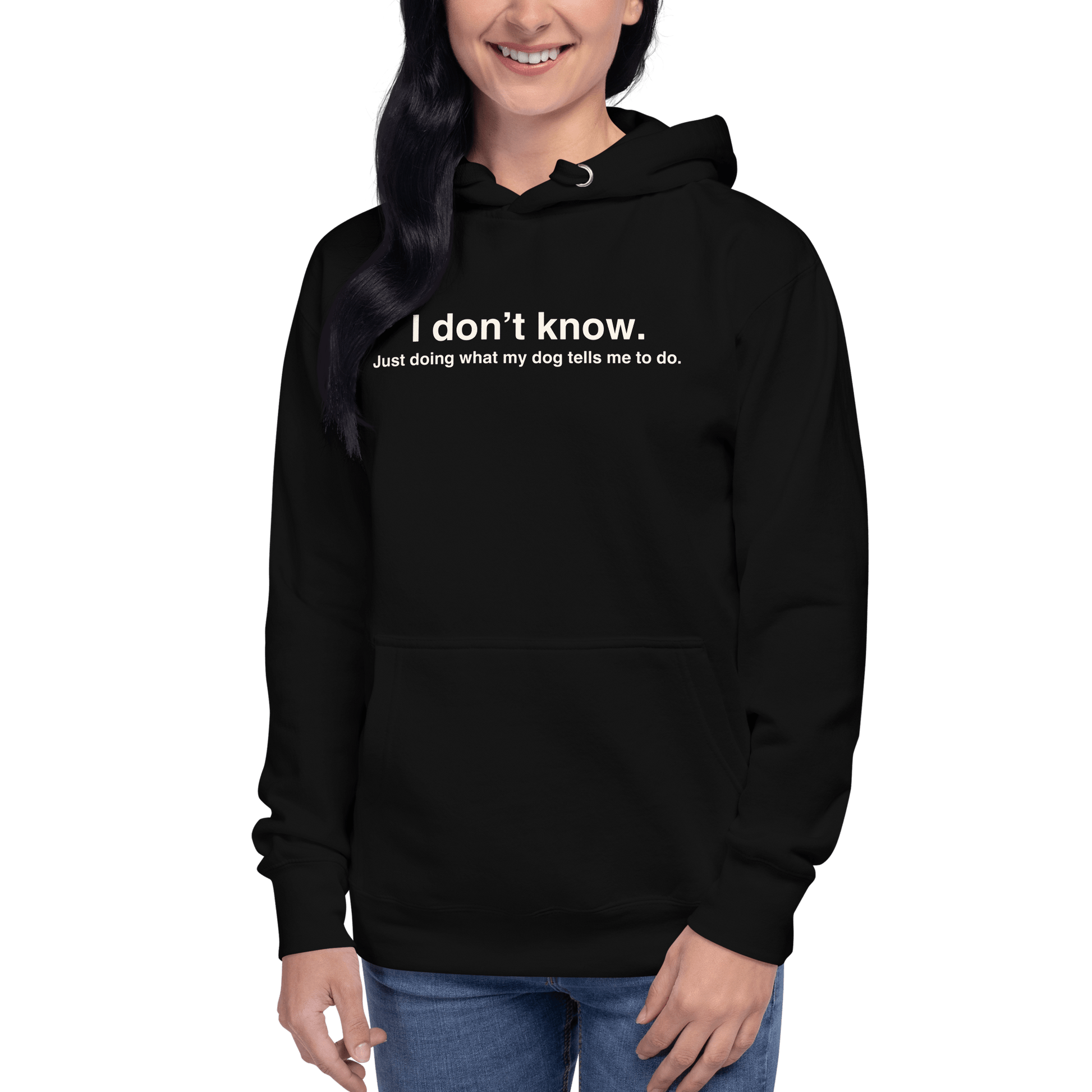 A woman wears the THiNK LiKE A DOG® Funny Dog Hoodie – Just Doing What My Dog Tells Me, a black unisex hoodie with the quote: "I don’t know. Just doing what my dog tells me to do."—an ideal gift for dog lovers—against a green background.