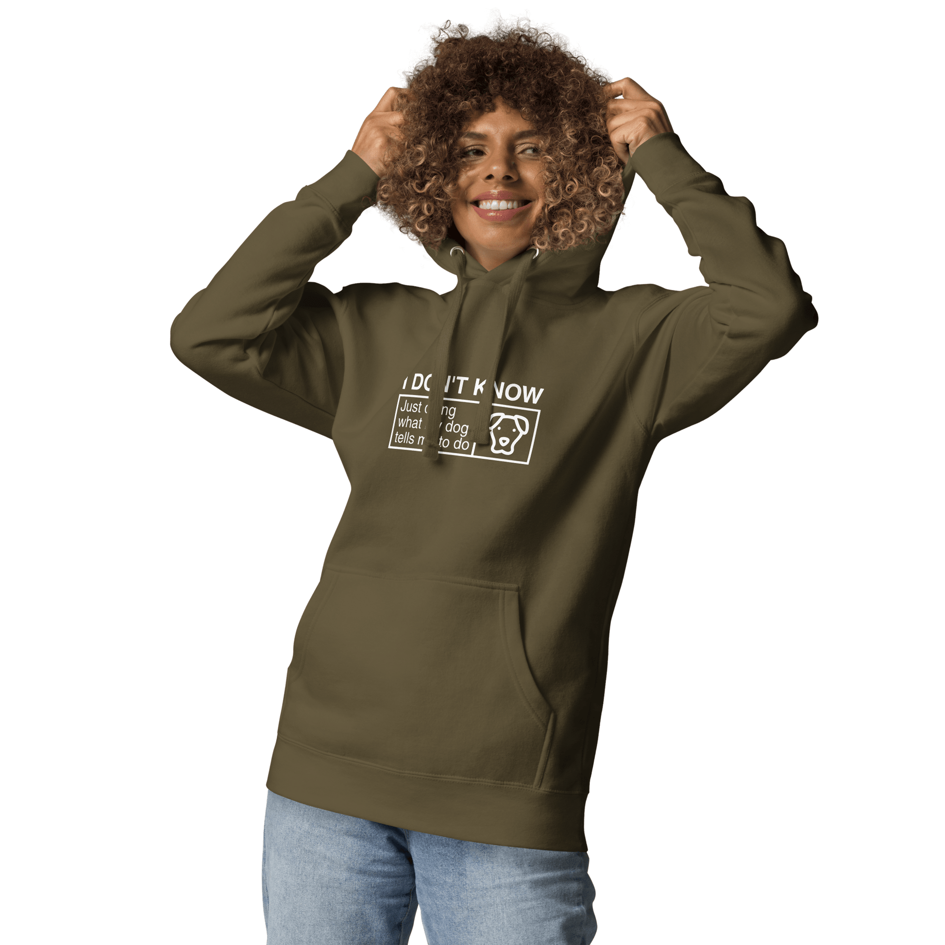 A person smiles and holds the hood of a green THiNK LiKE A DOG® hoodie with "I Don’t Know, Just Doing What My Dog Tells Me" text & dog graphic, paired with light blue jeans against a white background. This humorous dog-themed apparel is the perfect gift for dog lovers.