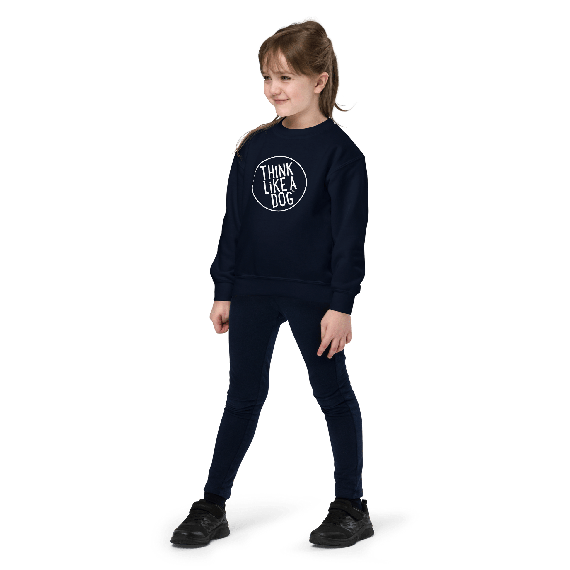 A young girl stands wearing the Kids' Cozy Crewneck Sweatshirt by THiNK LiKE A DOG®, featuring the brand's white logo. With her hair tied back, she gazes slightly to her left, radiating a vibe that’s unmistakably Dog-Lover Approved.