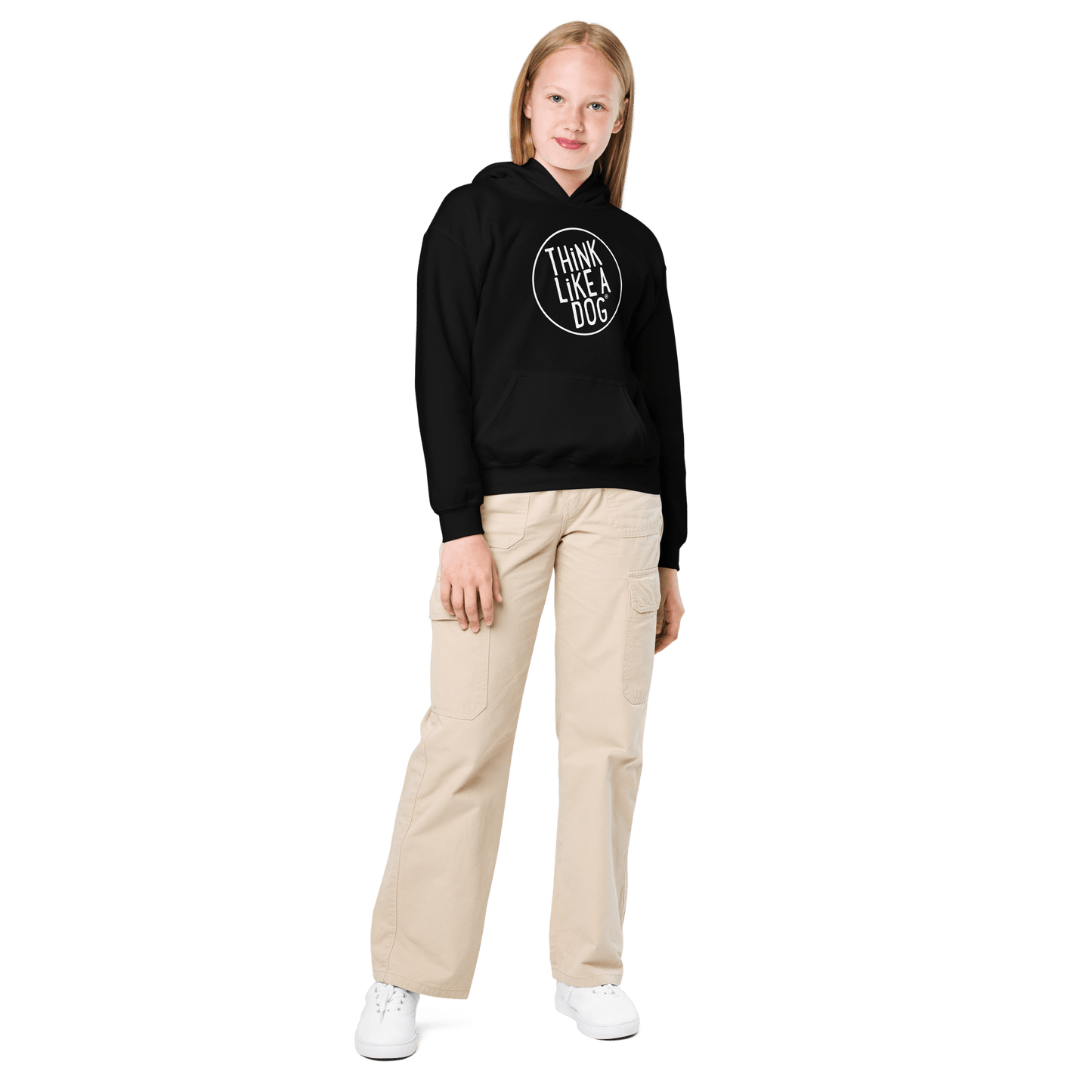 A child in a Kids Heavy Blend Hoodie with the THiNK LiKE A DOG® White Logo, beige cargo pants, and white sneakers stands against a black background, showcasing ultimate Dog-Lover Style.