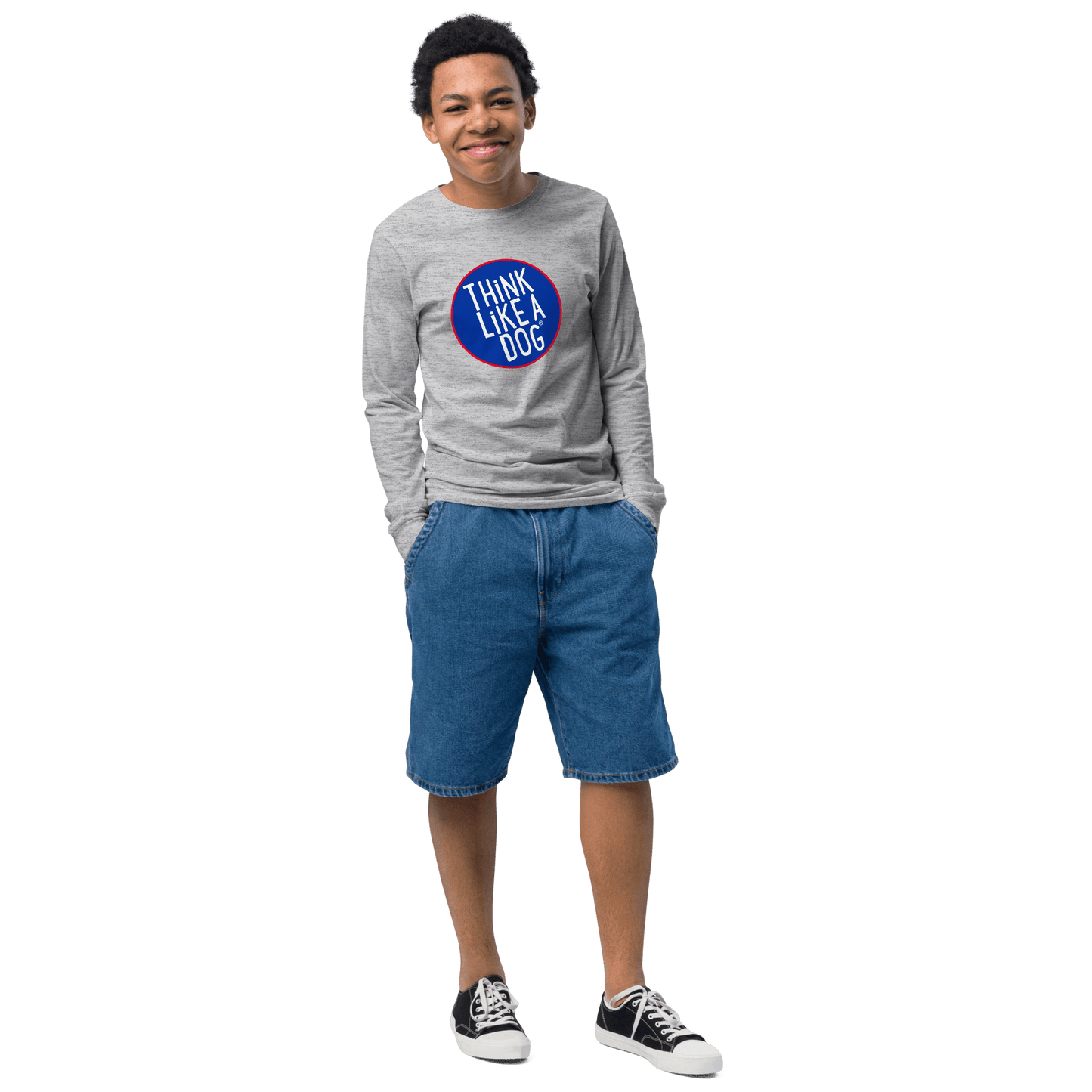 A person wearing a Kids' Think Like A Dog NASA-Style Long Sleeve Tee by THiNK LiKE A DOG®, with denim shorts and black sneakers, smiles with hands in pockets.