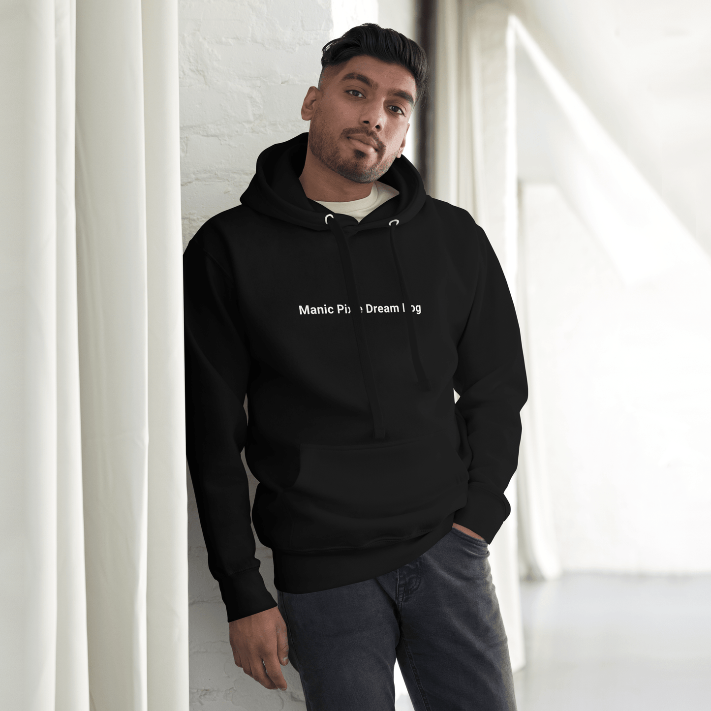 A person wearing a black Manic Pixie Dream Dog Hoodie by THiNK LiKE A DOG®, designed for dog lovers, stands against a white wall with curtains.