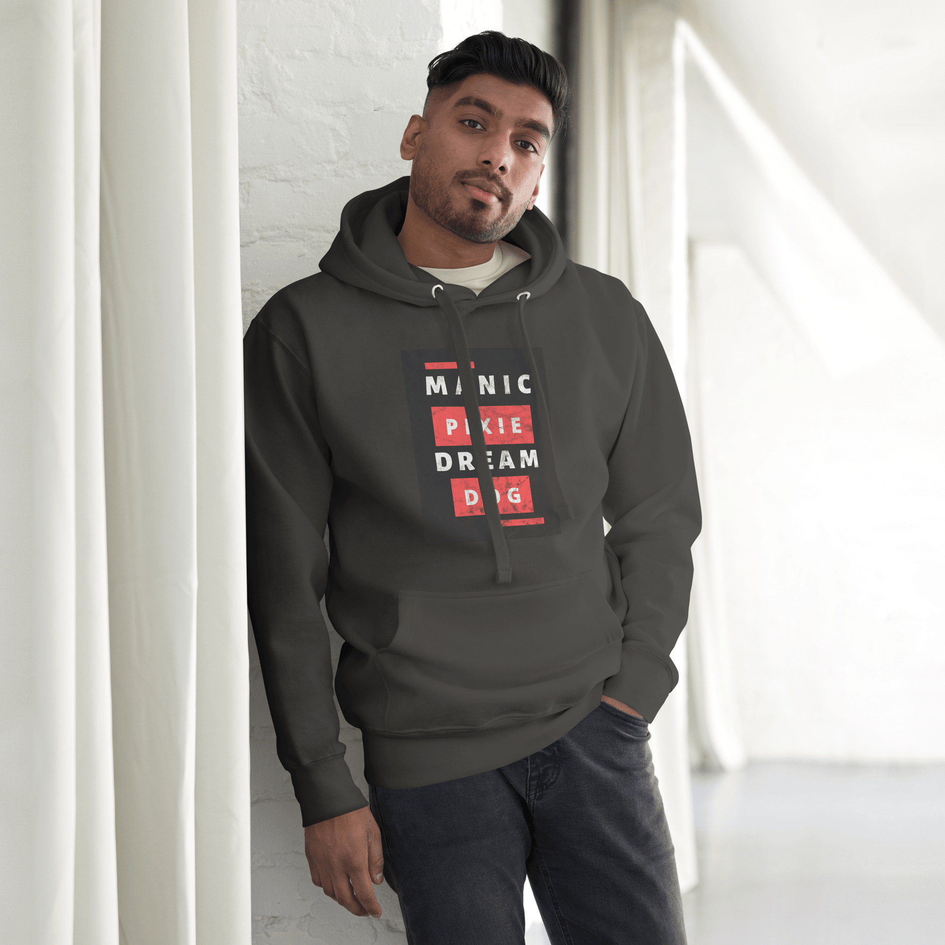 A person in a THiNK LiKE A DOG® Manic Pixie Dream Dog Hoodie, showcasing bold block-letter graphics, stands against a white brick wall in a well-lit room.