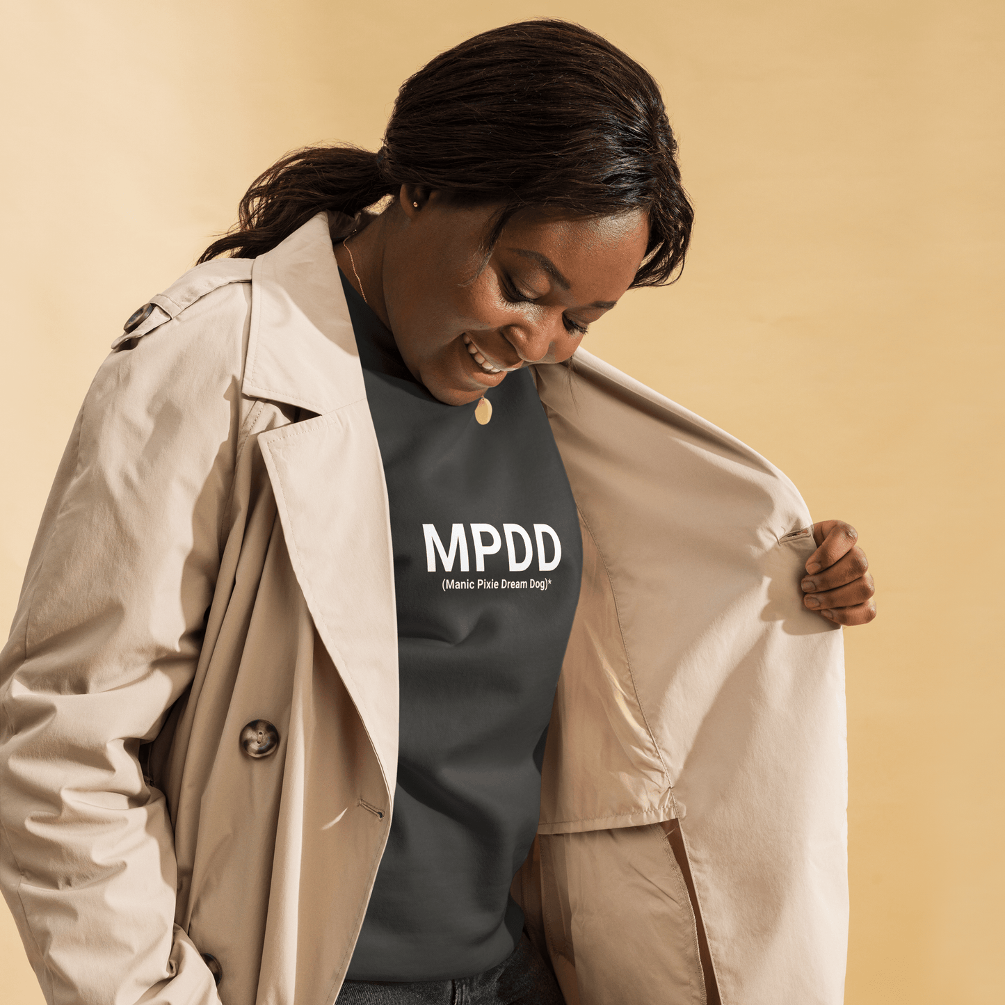 A woman smiles down, wearing a beige trench coat over the THiNK LiKE A DOG® Manic Pixie Dream Dog Definition Sweatshirt – Minimalist Comfort. This unisex sweatshirt is a perfect, thoughtful gift for pet lovers.