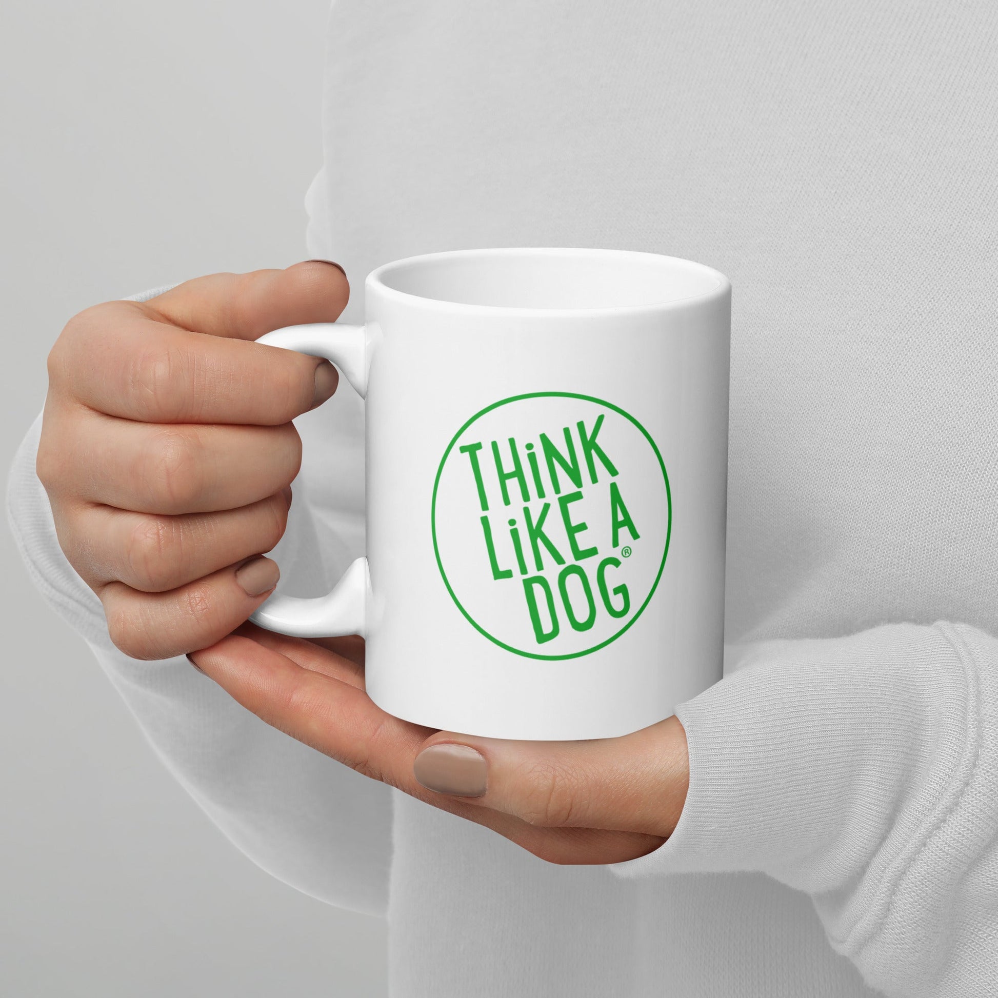 A person holding a white mug with their right hand. The mug has a text design that reads 'THINK LIKE A DOG' in bold, green letters inside a green circle outline.