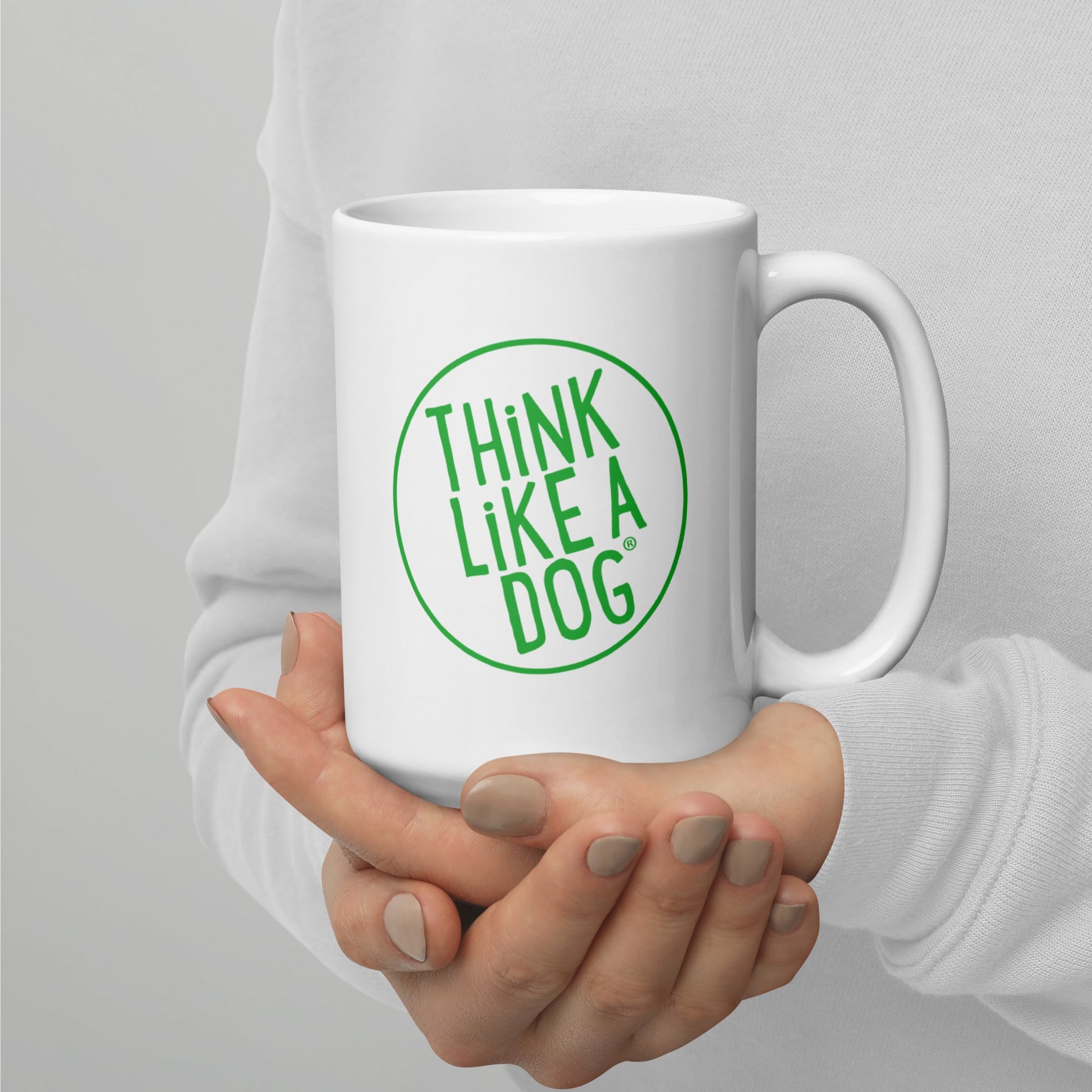 A person holding a white mug with their right hand. The mug has a text design that reads 'THINK LIKE A DOG' in bold, green letters inside a green circle outline.
