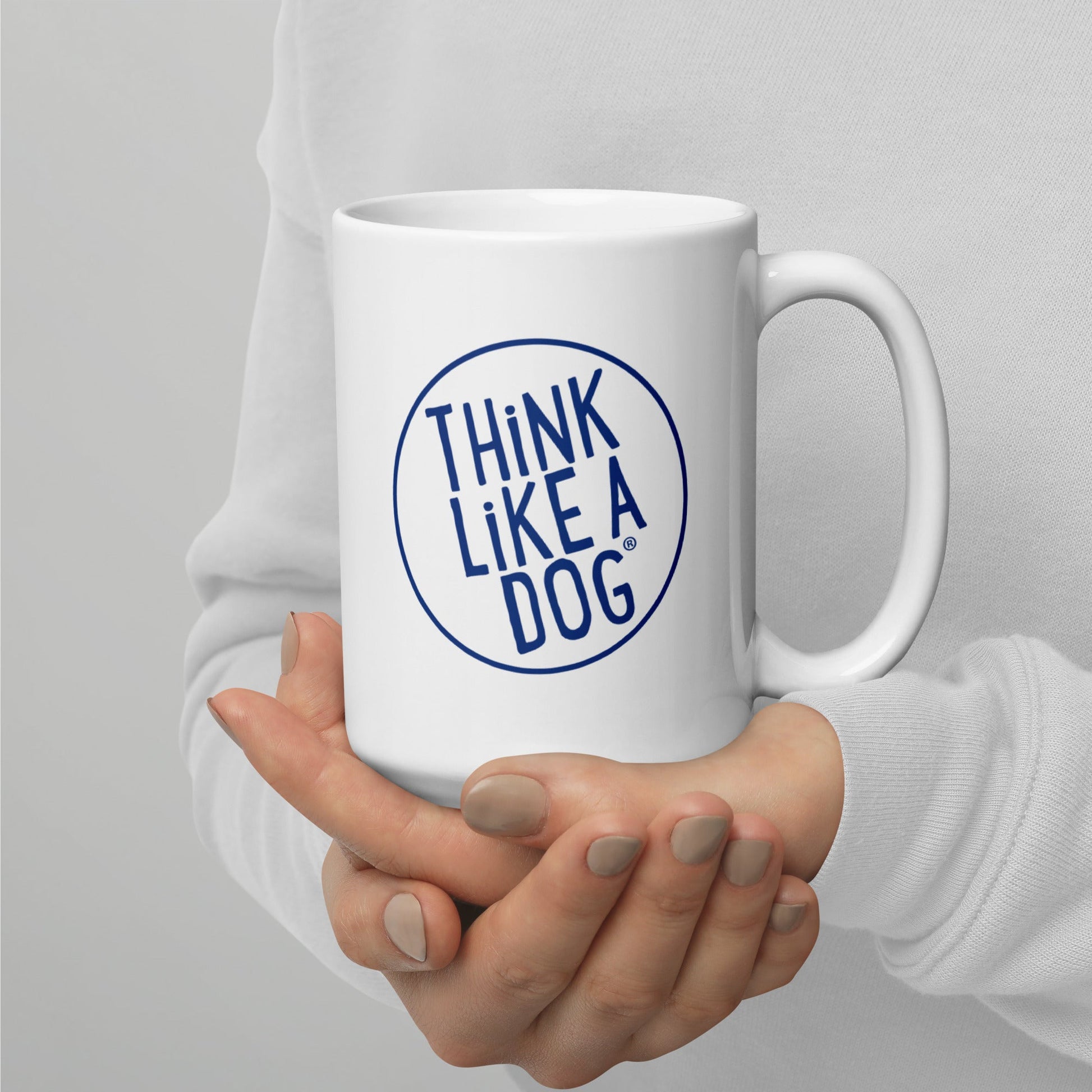 A person holding a THiNK LiKE A DOG® Dog Lover Mug – Think Like a Dog Navy Logo, featuring "THINK LIKE A DOG" in blue text inside a circle. The perfect dog mom gift.