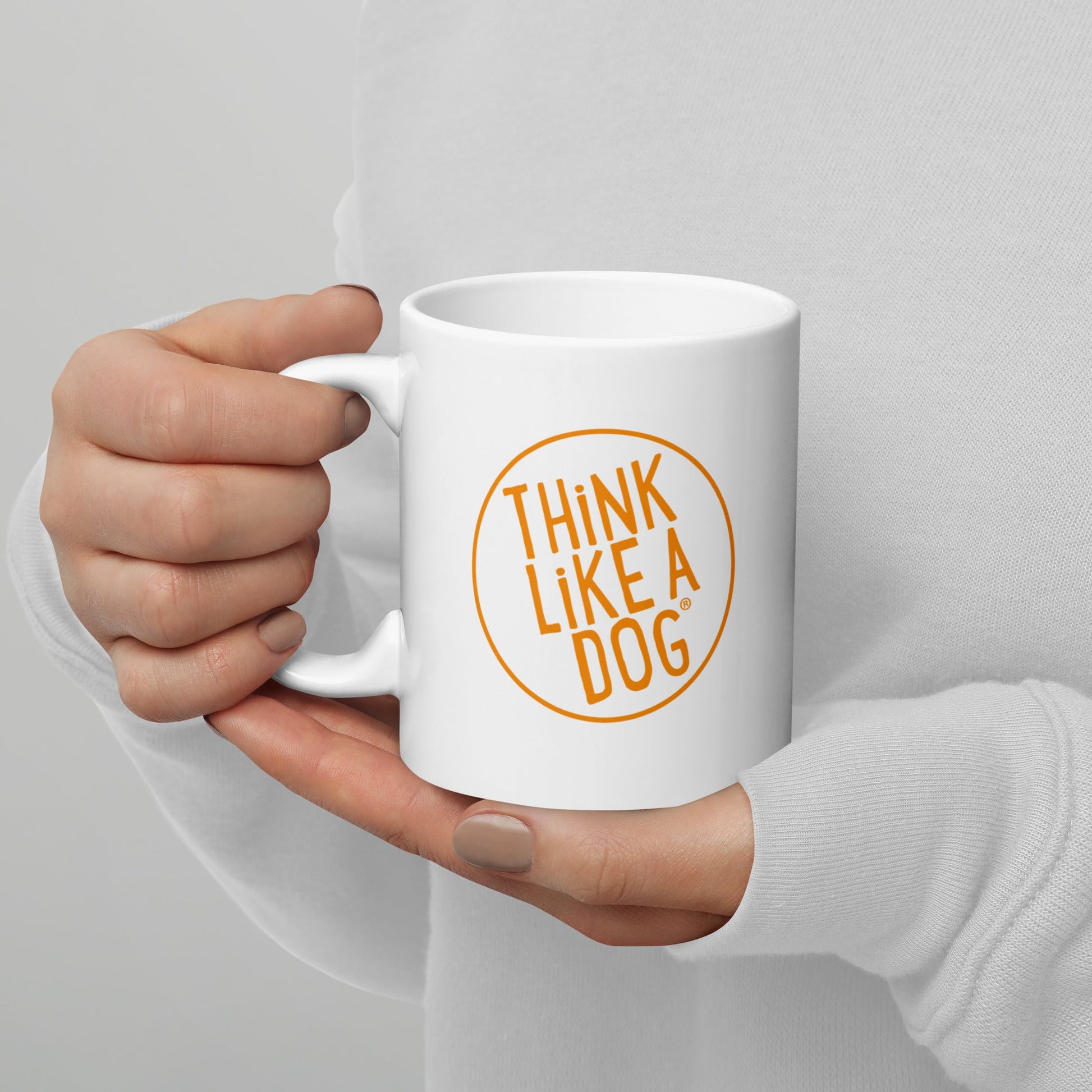 A person in a white sweater holds the THiNK LiKE A DOG® Think Like A Dog Mug – Vibrant Orange Logo, making it the perfect gift for any dog lover.