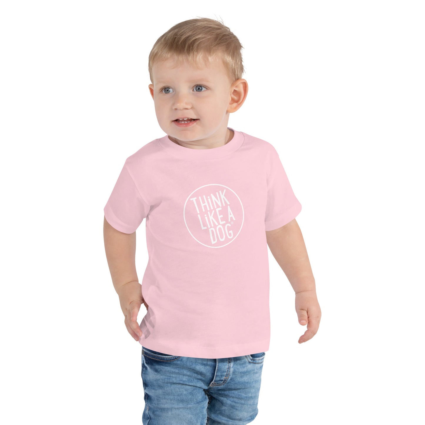 A cute toddler in a THiNK LiKE A DOG® ultra-soft tee, featuring the "THiNK LiKE A DOG" design, paired with blue jeans, stands against a white background.