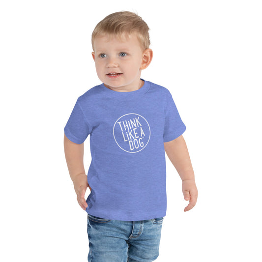 A young child wearing the THiNK LiKE A DOG® Toddler Short Sleeve Tee, known for being soft, playful, and inspiring, gazes adorably to the side while sporting this breathable blue tee.
