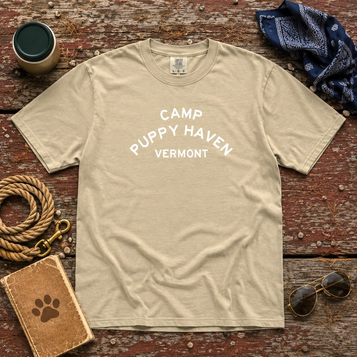 Camp Puppy Haven Vermont Tee in Khaki laid flat on weathered wood with a rope leash, navy bandana, thermos, aviators, and a paw-print notebook