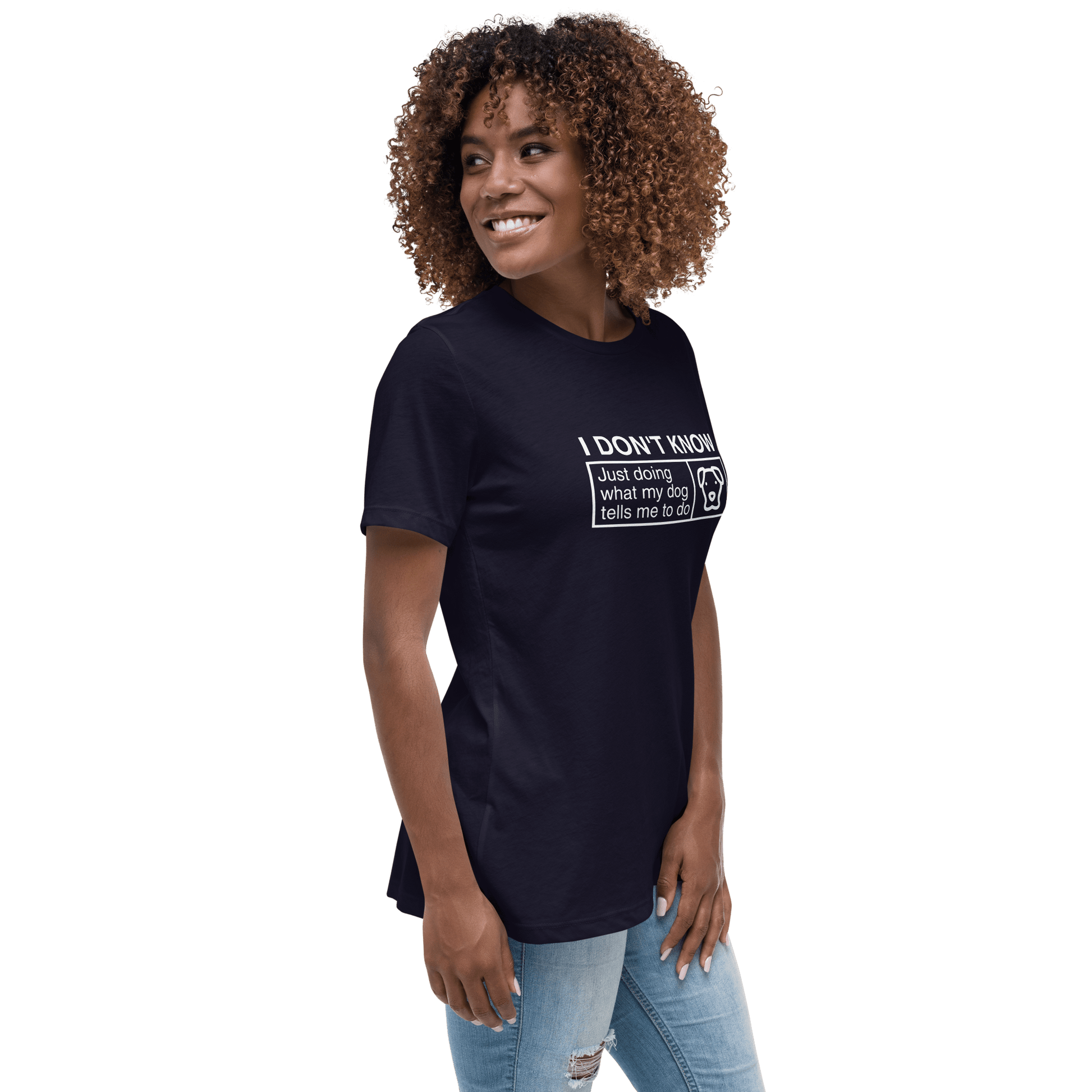 A curly-haired woman in a THiNK LiKE A DOG® navy tee that says, "Just Doing What My Dog Tells Me," smiles and glances sideways, pairing the funny dog shirt perfectly with her ripped jeans.