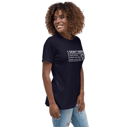 A curly-haired woman in a THiNK LiKE A DOG® navy tee that says, "Just Doing What My Dog Tells Me," smiles and glances sideways, pairing the funny dog shirt perfectly with her ripped jeans.