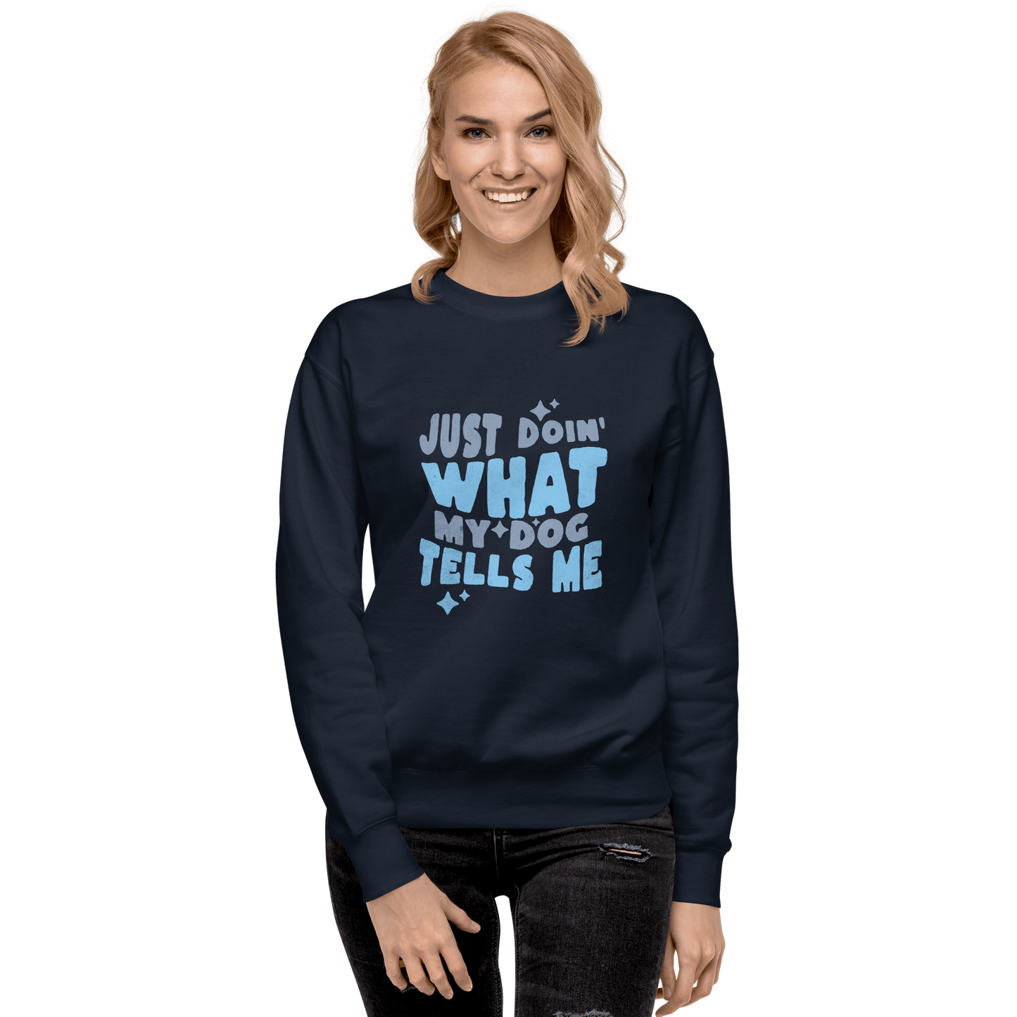 A smiling person with long blonde hair wears the THiNK LiKE A DOG® Funny Dog Sweatshirt—Doing What My Dog Tells Me, a cozy navy unisex crewneck with "Just doin' what my dog tells me" printed in blue letters.