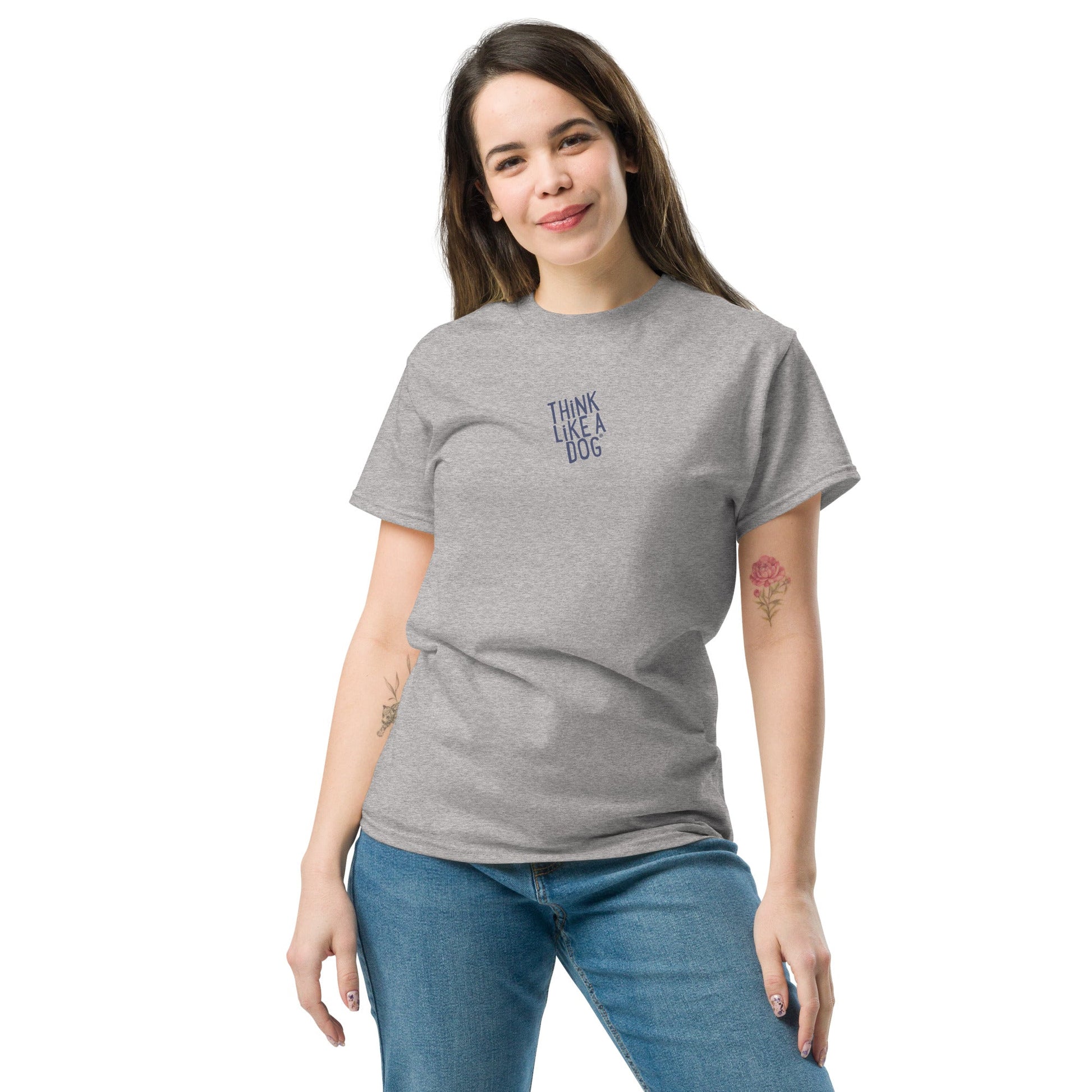 A woman smiles in blue jeans and a THiNK LiKE A DOG® Think Like a Dog T‑Shirt — Everyday Comfort, featuring the slogan "THINK LIKE A DOG," against a white background.