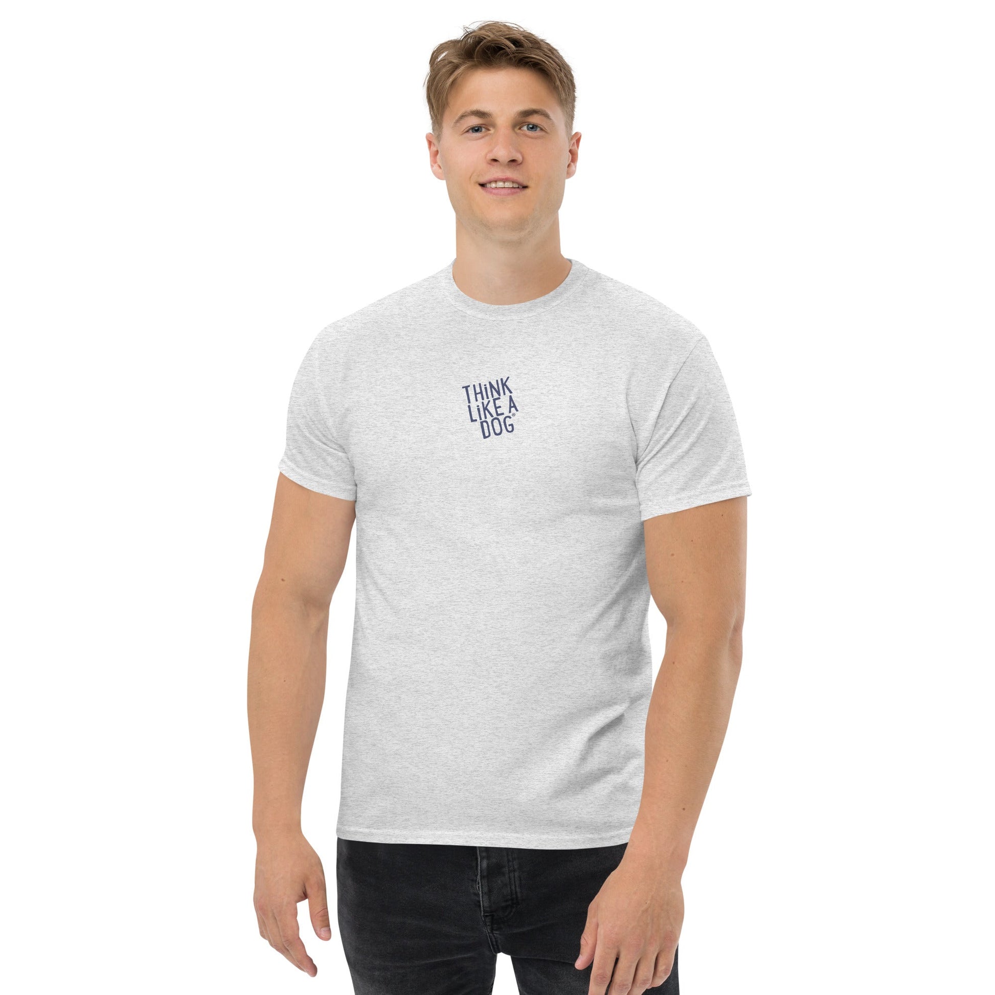 A man wears a THiNK LiKE A DOG® Think Like a Dog T-Shirt – Sport Grey Logo, featuring "THINK LIKE A DOG" text on the upper left chest, standing against a plain background.