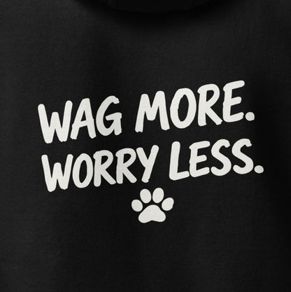 Close-up of the Wag More. Worry Less. back print — white hand-lettered slogan and small paw on black fleece.