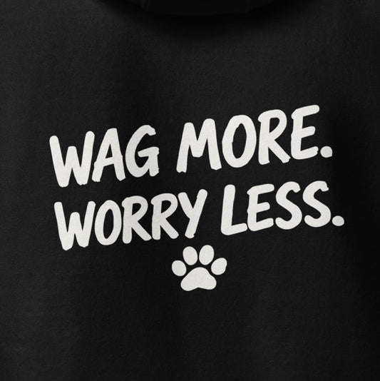 Close-up of the Wag More. Worry Less. back print — white hand-lettered slogan and small paw on black fleece.