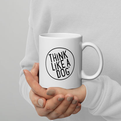 A person holding a white mug with their right hand. The mug has a text design that reads 'THINK LIKE A DOG' in bold, black letters inside a black circle outline.