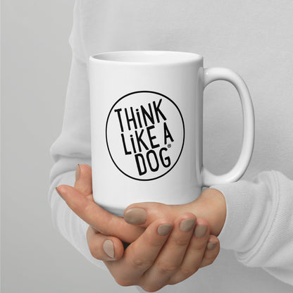 A person holding a white mug with their right hand. The mug has a text design that reads 'THINK LIKE A DOG' in bold, black letters inside a black circle outline.