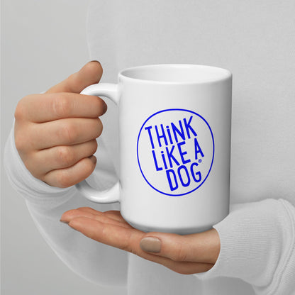 A person holding a white mug with their right hand. The mug has a text design that reads 'THINK LIKE A DOG' in bold, blue letters inside a blue circle outline.