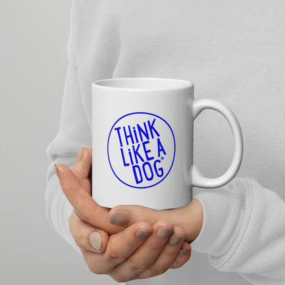 A person holding a white mug with their right hand. The mug has a text design that reads 'THINK LIKE A DOG' in bold, blue letters inside a blue circle outline.
