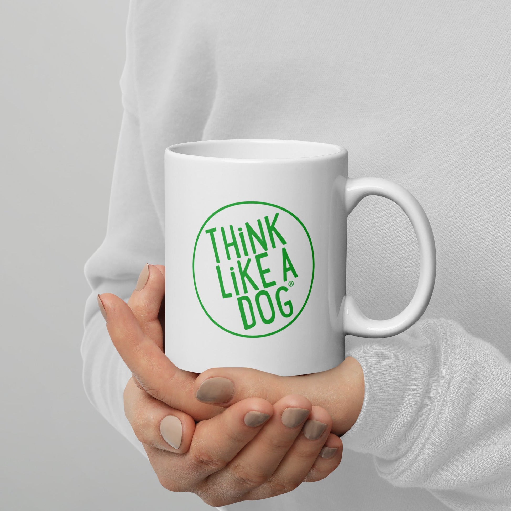 A person holding a white mug with their right hand. The mug has a text design that reads 'THINK LIKE A DOG' in bold, green letters inside a green circle outline.