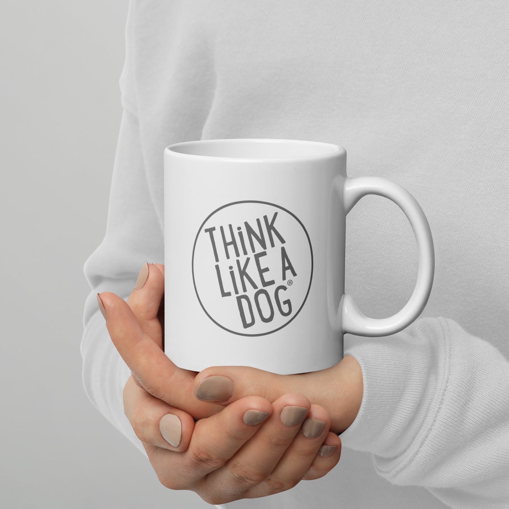 Person holding a White Glossy Mug Grey THiNK LiKE A DOG® Logo, perfect for dog lovers.