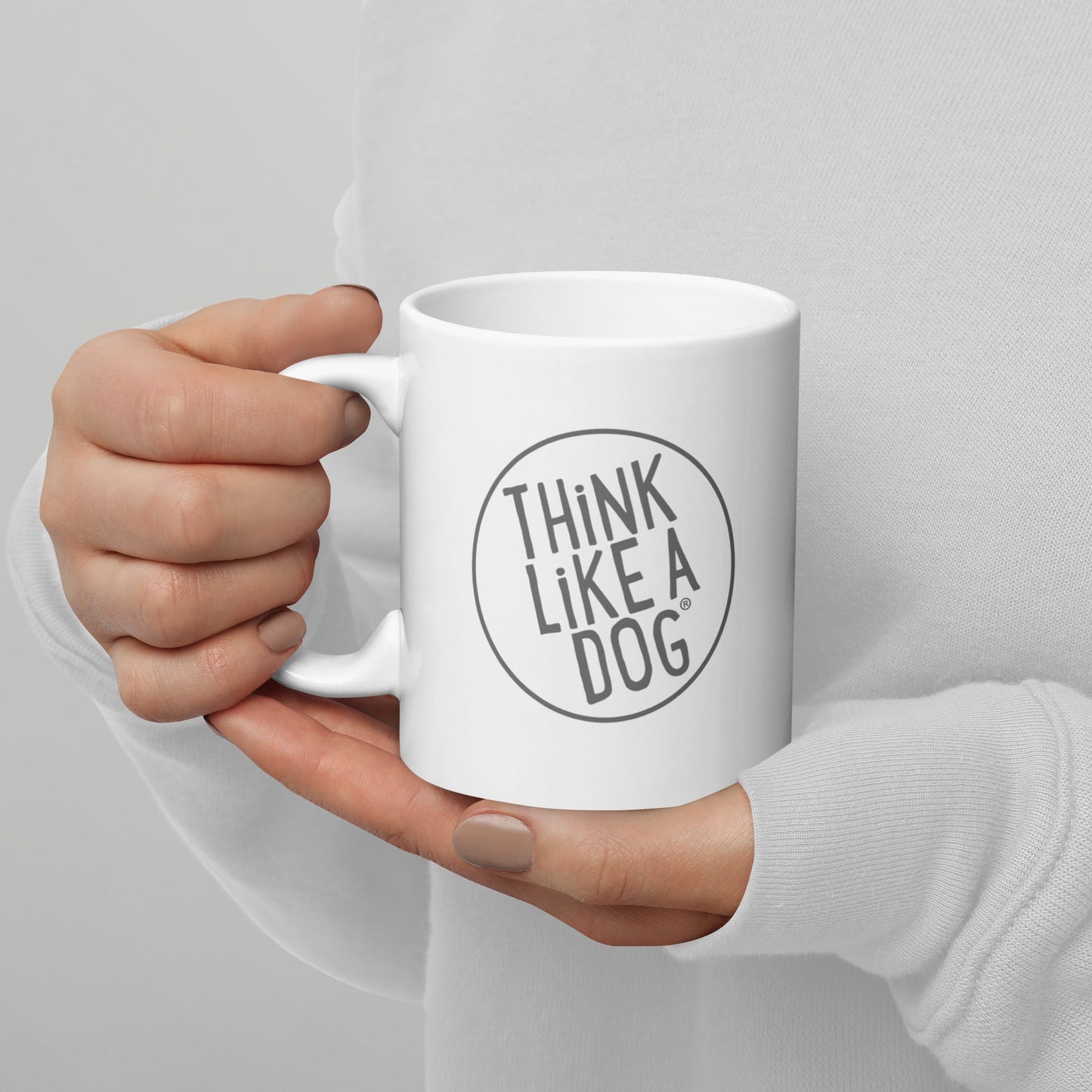 A person holding a White Glossy Mug Grey THiNK LiKE A DOG® Logo with the inscription "Think Like a Dog".
