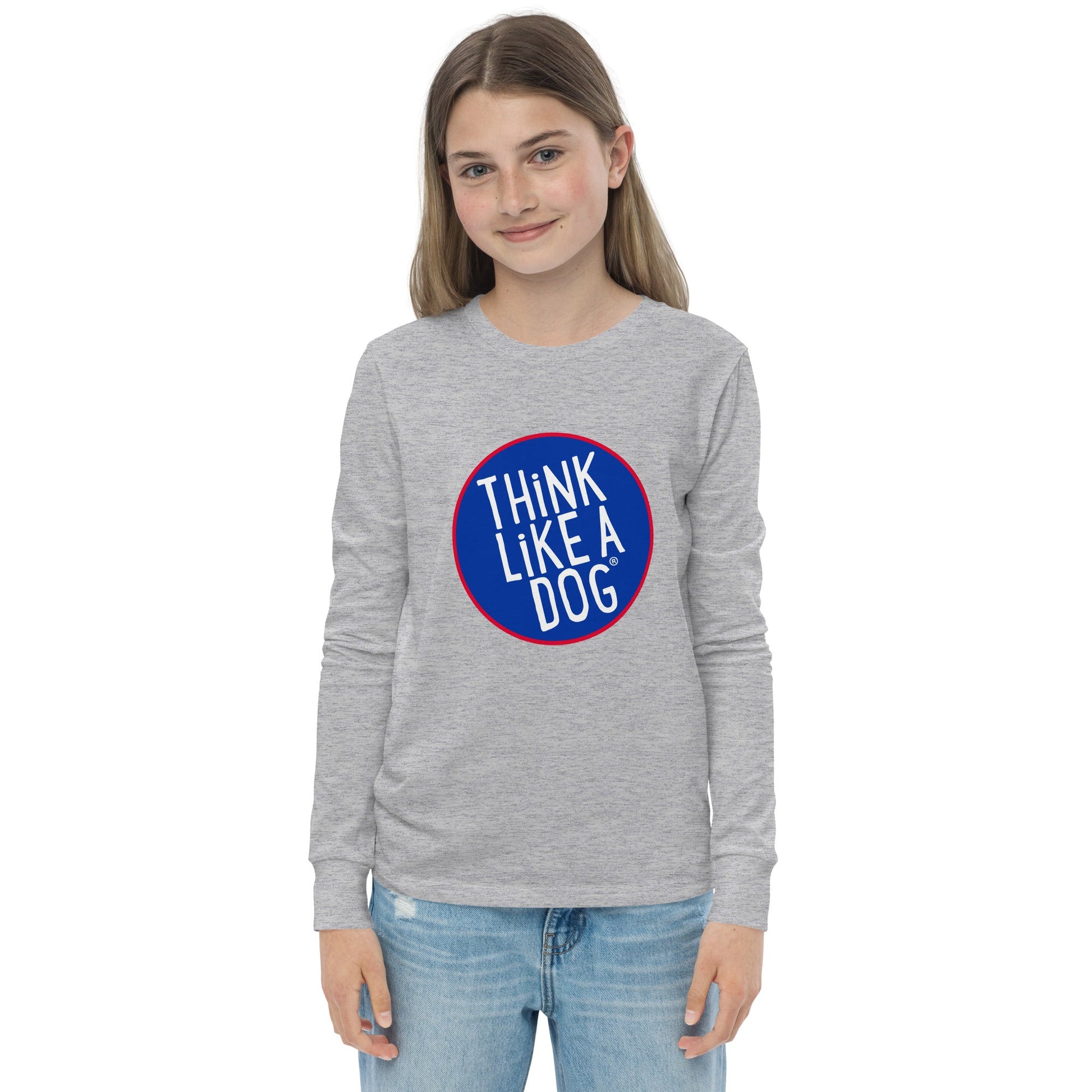 A young dog-loving kid stands against a plain background, wearing the THiNK LiKE A DOG® Kids' Think Like A Dog NASA-Style Long Sleeve Tee with blue jeans. This fun canine-inspired shirt captures the adventurous spirit of aspiring kids with its quirky charm.