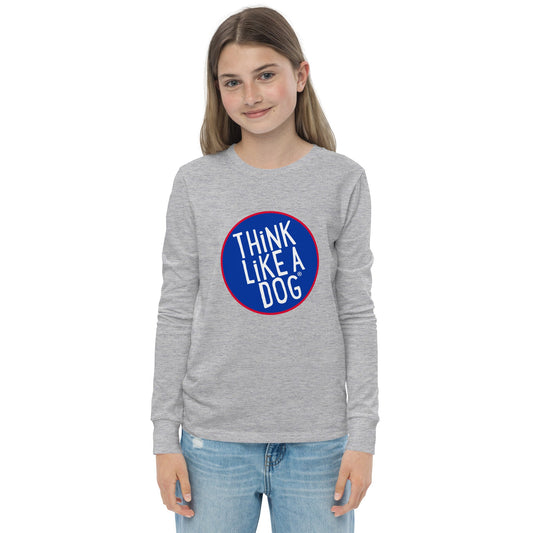 A young person with long hair is wearing the THiNK LiKE A DOG® Kids' Think Like A Dog NASA-Style Long Sleeve Tee - Cute and Quirky Dog Apparel, crafted from high-quality soft fabric. The gray shirt showcases a blue and red circular design that reads "THINK LIKE A DOG.