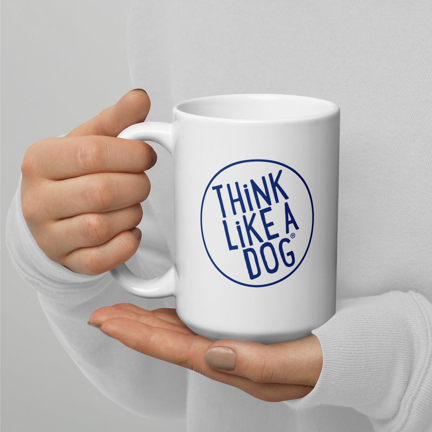 Person holding a THiNK LiKE A DOG® white glossy mug with the phrase "THiNK LiKE A DOG®" printed in blue, designed for dog lovers.