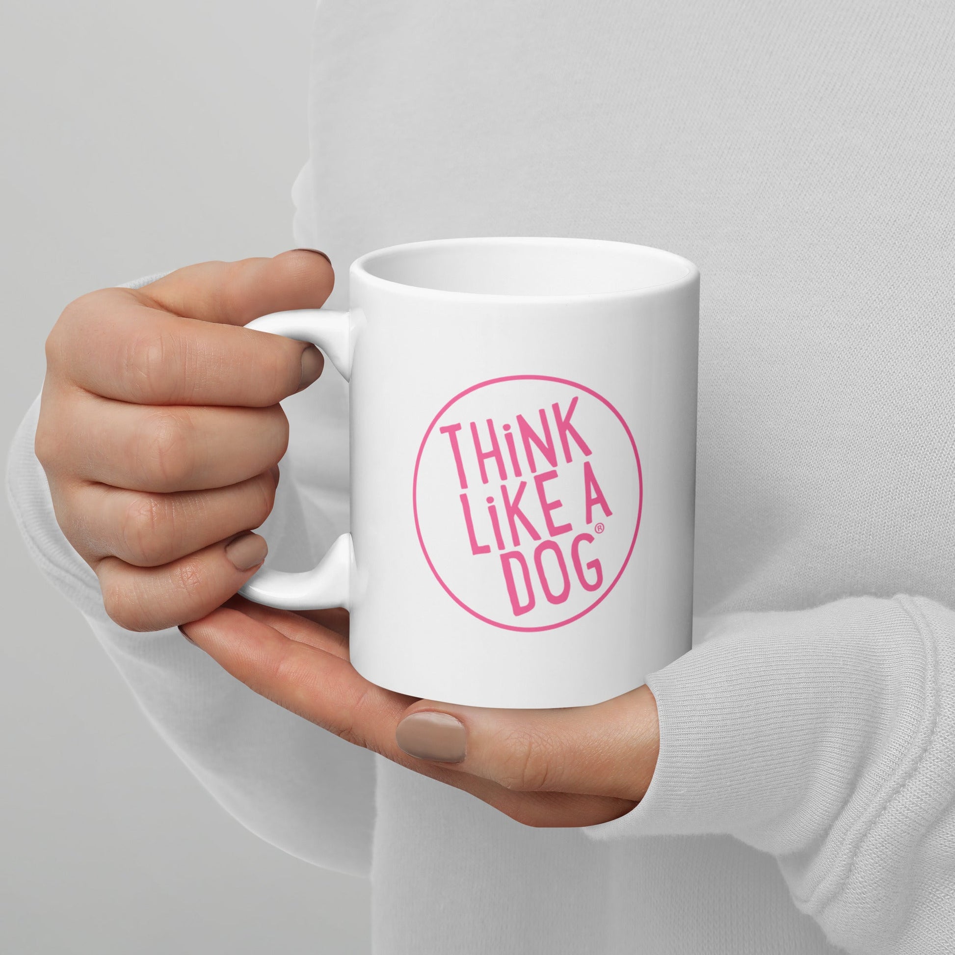 A person holding a white mug with their right hand. The mug has a text design that reads 'THINK LIKE A DOG' in bold, pink letters inside a pink circle outline.
