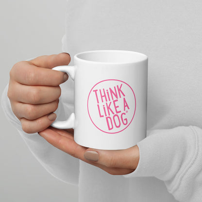 A person holding a white mug with their right hand. The mug has a text design that reads 'THINK LIKE A DOG' in bold, pink letters inside a pink circle outline.