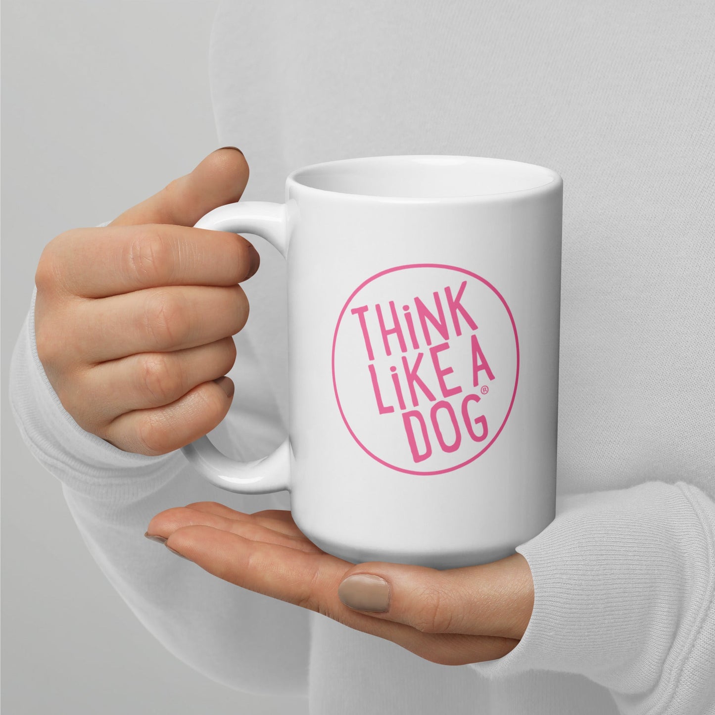 A person holding a white mug with their right hand. The mug has a text design that reads 'THINK LIKE A DOG' in bold, pink letters inside a pink circle outline.