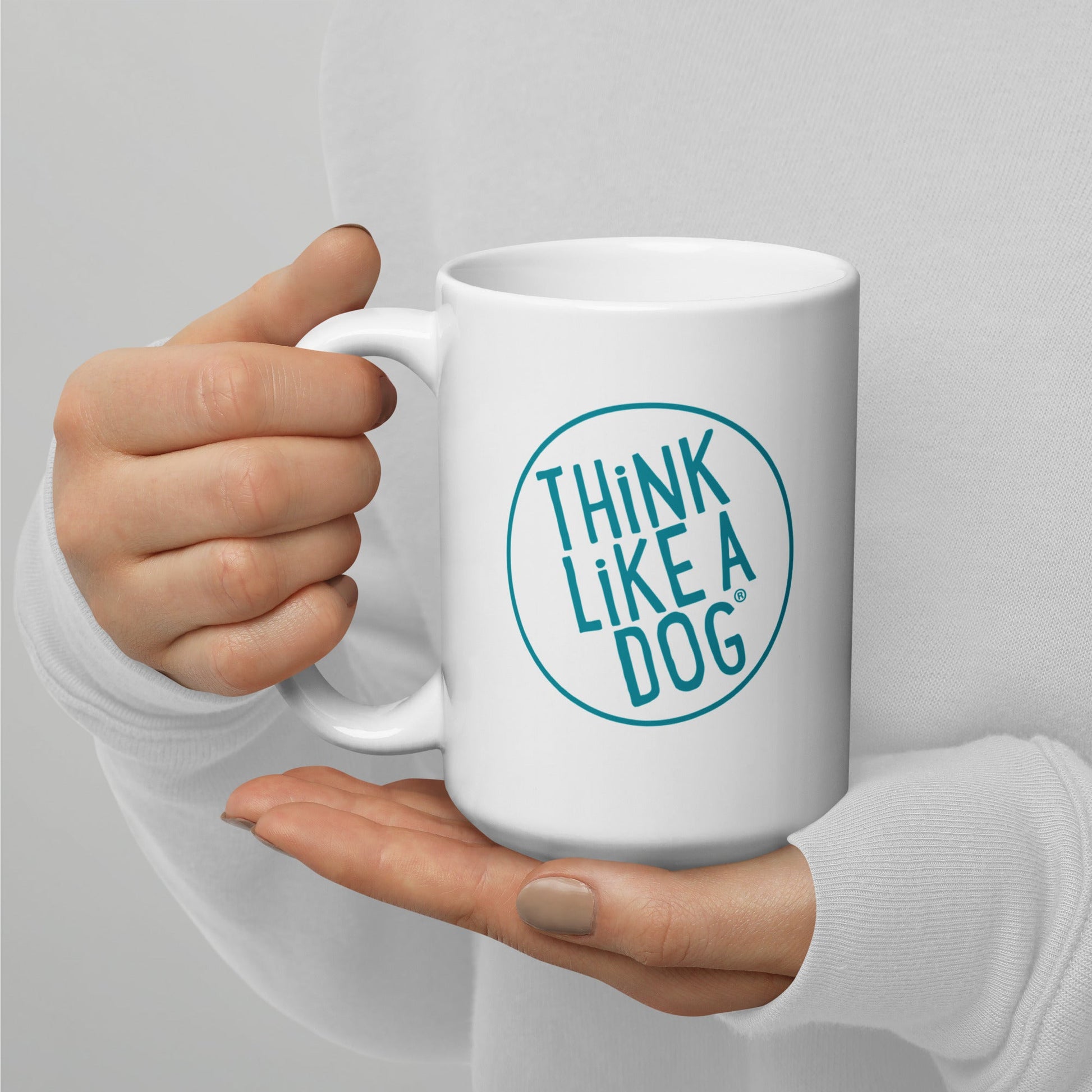 A person holding a White Glossy Mug Teal THiNK LiKE A DOG® Logo with the phrase "THiNK LiKE A DOG®" printed on it, perfect for dog lovers.